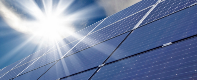 Image of solar panels with bright sunlight reflecting off them against a partly cloudy sky.